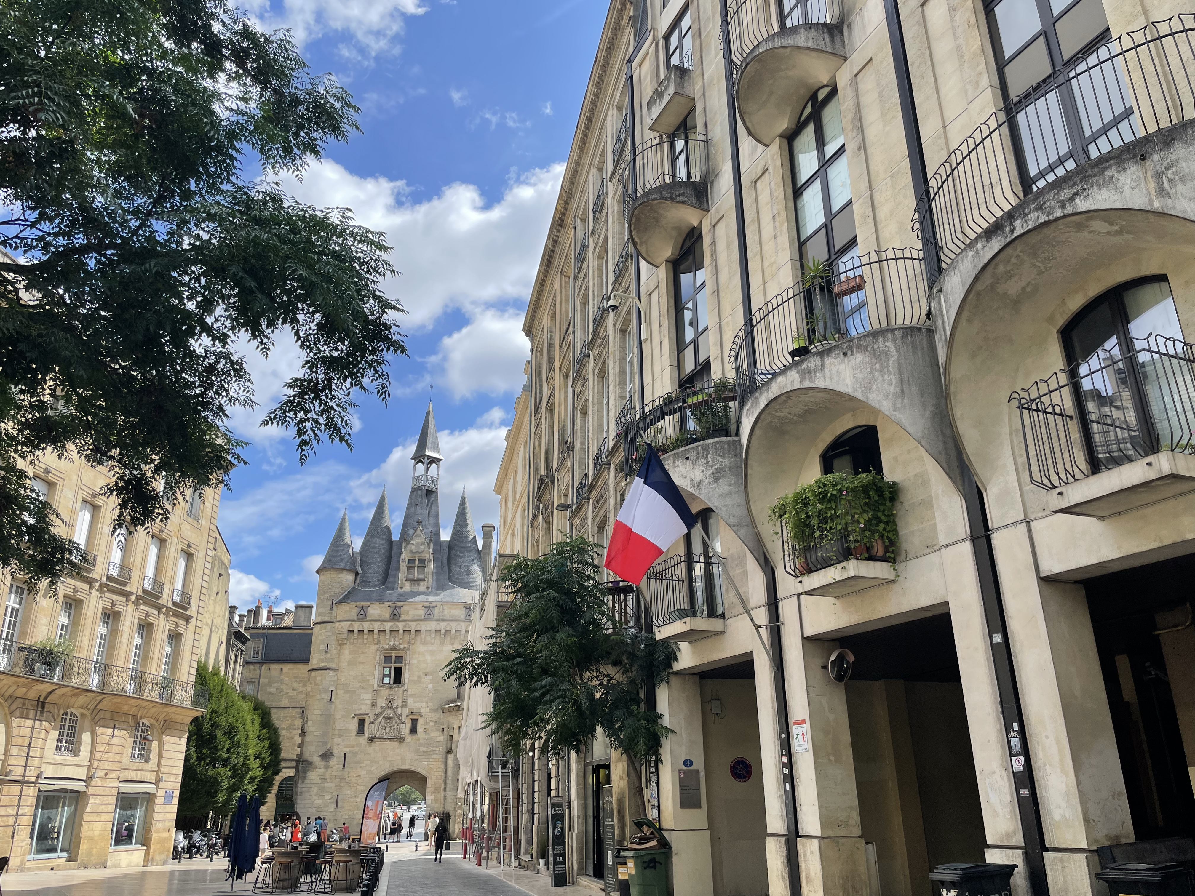 street with French flag behind Porte Cailhau, a castle-like gate in Bordeaux