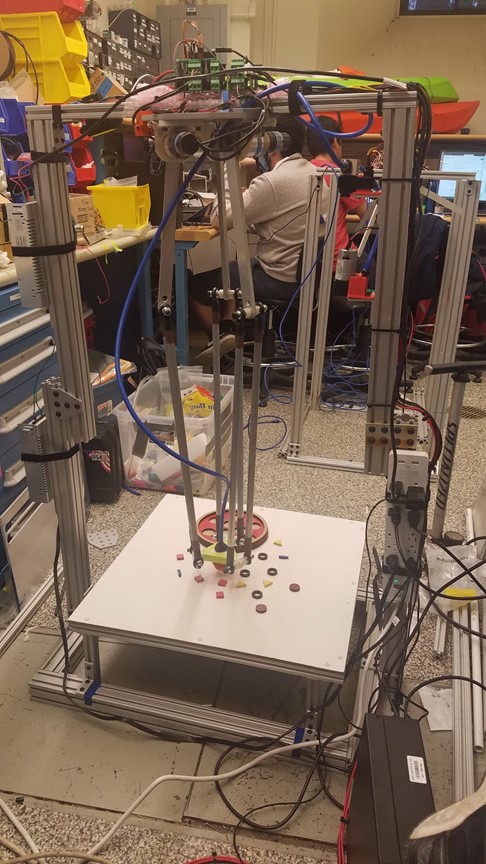 Delta robot with metal frame and linkages surrounding a table with fake pizza within the lab.