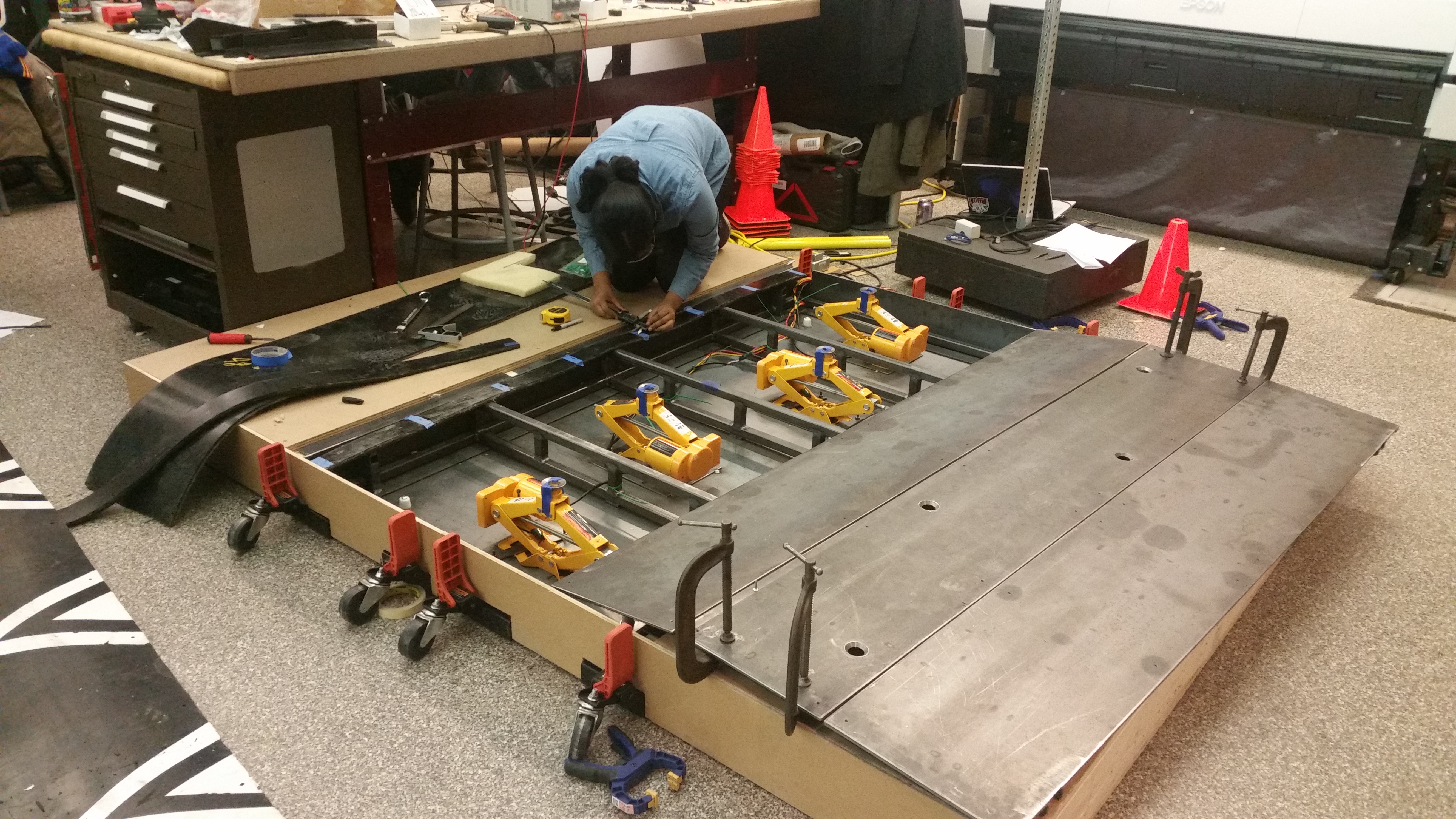 The speed bump sits in a wooden case meant to represent excavated road. I am measuring a width on the side. The steel plates from the top are off and you can see the four car jacks.